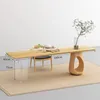 A wooden dining table with a modern design, shown in a minimalist setting with a chair and tea set. Produktbild-Vorschau
