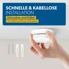 A hand is holding a smoke detector near a ceiling, with screws and wall plugs visible below. Produktbild-Vorschau