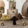 A dark brown paper mushroom decoration sits on a wooden surface, surrounded by natural elements like hazelnuts and dried flowers. Produktbild-Vorschau