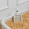 A close-up view of a white cat litter box filled with wood pellet litter, with a white litter scoop resting inside. Voir les images du produit