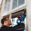 A man is using a reciprocating saw to remove a window frame. Anteprima dell’immagine prodotto