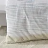A close-up view of a striped duvet cover with a beige bottom edge, resting on a fluffy white rug. Produktbild-Vorschau