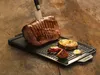 A grilled steak and vegetables on a grill plate on a wooden surface. Anteprima dell’immagine prodotto