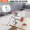 A stainless steel meat grinder is shown on a wooden table in a kitchen setting. It is actively grinding meat, with some meat in the hopper and ground meat on a plate. Náhľad obrázku produktu