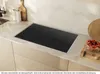A black induction cooktop with a silver frame is shown on a kitchen countertop. Náhľad obrázku produktu