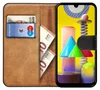A book-style phone case with a Samsung Galaxy M31 inside, displaying a colorful abstract wallpaper. The case also holds a bank card and euro banknotes. Náhľad obrázku produktu