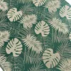 A close-up view of a green tablecloth with a repeating pattern of beige monstera and palm leaves. Produktbild-Vorschau