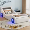 A child's bed designed in the shape of a car, with decorative pillows and a rug with toy trains. Produktbild-Vorschau
