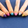 A close-up shot of the tips of six colored pencils arranged in a semi-circle on a dark blue surface. Voir les images du produit