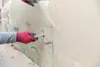 A person wearing red gloves is applying a layer of mortar to a wall with a trowel. Produktbild-Vorschau