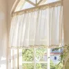 A sheer curtain with a diamond pattern and tassels hangs in a window. Produktbild-Vorschau