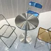 A round metal table with three chairs around it. The chairs have transparent frames and colored seats/backs. Produktbild-Vorschau
