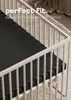 A close-up view of a black fitted sheet on a white crib mattress, with the crib railings visible. Produktbild-Vorschau