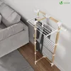 A drying rack with clothes is placed next to a sofa in a room. Produktbild-Vorschau