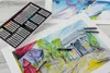 A box of oil pastels and several drawings are laid out on a table. Podgląd zdjęcia produktu