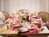 A beautifully set table for a tea party or breakfast, featuring delicate floral patterned tableware, fresh strawberries, and colorful flowers. Anteprima dell’immagine prodotto