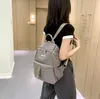 A woman wearing a black and white shirt and gray pants walks down a hallway, carrying a gray backpack. Podgląd zdjęcia produktu