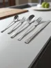 A set of stainless steel cutlery is laid out on a countertop. Anteprima dell’immagine prodotto