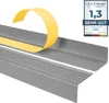 A close-up of a gray stair nosing profile with yellow adhesive tape being peeled off, and a certification badge in the upper right corner. Anteprima dell’immagine prodotto