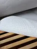 A white mattress topper with raised dots rests on wooden slats of a bed frame. Produktbild-Vorschau
