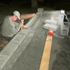 A man is working on a construction project, laying down concrete blocks and using tools. The scene is outdoors at night, illuminated by artificial lights. Náhled obrázku produktu