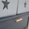A close-up view of a gray dresser with a wooden handle and two fabric storage boxes with star cutouts on top. Produktbild-Vorschau