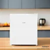 A white mini refrigerator is placed on a wooden countertop in a kitchen setting. Produktbild-Vorschau
