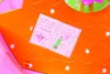 A close-up of a toy cottage with a drawing of a bee and a flower in a notebook. Produktbild-Vorschau