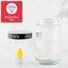 A product shot featuring a solar-powered LED grave light and a separate glass jar, set against a light marble-patterned background. Produktbild-Vorschau