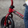 Close-up of a red balance bike with a child's leg visible. Produktbild-Vorschau