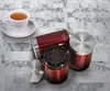 A white teacup and saucer sit next to three red storage containers labeled 'Coffee', 'Tea', and 'Sugar' on a marble-like surface. Voir les images du produit