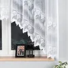A close-up view of a white lace curtain hanging over a window, with a framed photo and a lantern on the windowsill. Produktbild-Vorschau