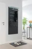 A modern entryway with a black coat rack panel mounted on a light gray wall, featuring hooks for hats and scarves, a glass shelf, and a pair of sneakers on a doormat. Produktbild-Vorschau