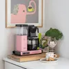 A pink Moccacoffee machine is displayed on a wooden board on a countertop, with a framed artwork of a pink elephant in the background. Náhľad obrázku produktu