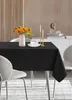 A black tablecloth is laid out on a dining table, set with a vase of orange flowers, a cup of coffee, and two candles. Produktbild-Vorschau