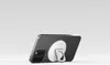 A black iPhone with a white MagSafe accessory attached to the back is shown from a side-angle, resting on a white surface. Produktbild-Vorschau