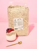 A large bag of oat flakes stands behind a glass of yogurt topped with berries, with a golden spoon in the foreground, all set against a pink background. Produktbild-Vorschau