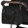 A black diaper bag is attached to the handle of a stroller. Produktbild-Vorschau