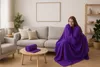A woman is sitting on a couch wrapped in a purple blanket in a living room. Produktbild-Vorschau