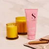 A pink tube of hair conditioner sits next to two yellow candles on a marble surface. Produktbild-Vorschau