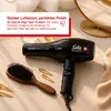 A black Solis hairdryer with a wooden hairbrush and gold hair clips on a light-colored surface, with a blurred background of cosmetic items and a mirror. Produktbild-Vorschau