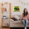 A woman is sitting on a couch next to a shelf with various items, with a sign on the wall behind her. Produktbild-Vorschau