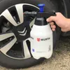 A hand holds a white spray bottle with a black and blue pump mechanism in front of a car wheel. Produktbild-Vorschau