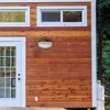 Close-up of the exterior of a wooden tiny house, showing a door, windows, and an outdoor light fixture. Podgląd zdjęcia produktu