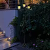 A solar-powered street lamp with three lights stands in a garden at dusk, illuminating a stone staircase and surrounding greenery. Produktbild-Vorschau