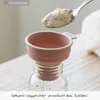 A pink silicone funnel is placed on a glass baby bottle, with a spoon of powder being poured into the funnel. Anteprima dell’immagine prodotto