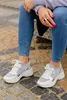 A person is sitting outdoors on a stone bench, wearing jeans and sneakers. Produktbild-Vorschau