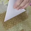 A hand is shown using a white tool to peel back a protective film from a diamond painting kit. Produktbild-Vorschau