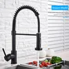 A black kitchen faucet with a coiled hose is shown in a kitchen sink with vegetables. Náhled obrázku produktu