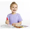 A young girl is sitting at a table and drawing with crayons and markers. Podgląd zdjęcia produktu